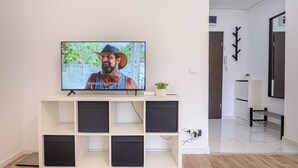 A modern living room with a flat-screen TV on a white entertainment unit, a plant on the unit, and a hallway leading to another room. - Deda Studio w. Smart TV · AC · washing machine (Bucharest)