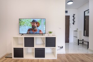 A modern living room with a flat-screen TV on a white entertainment unit, a plant on the unit, and a hallway leading to another room. - Deda Studio w. Smart TV · AC · washing machine (Bucharest)