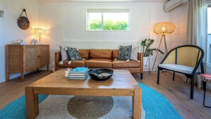 Een woonkamer met een bruine leren bank, een houten bijzettafeltje, een rieten vloerlamp en een rotan kast.