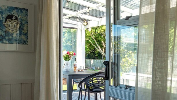 Een conservatorium met een glazen deur die leidt naar een terras, een tafel met stoelen en een lijst met een kunstwerk aan de muur.