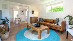Een woonkamer met een houten salontafel, een bruine leren bank en een blauw vloerkleed.