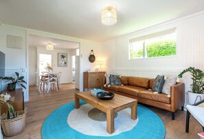 A living room with a wooden coffee table, a brown leather sofa, and a blue rug. - Bach 14 – Relaxed Family Escape in Blackpool (Waiheke Island)