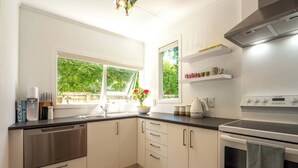 Een moderne keuken met witte kastjes, een vaatwasser, een oven en een raam met uitzicht op groen.