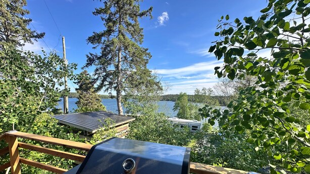 Ein Grill auf einer Terrasse mit Blick auf einen See, Bäume und ein Boot im Hintergrund.