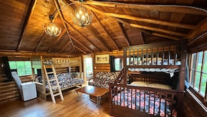 Ein Interieur einer Holzhütte mit Holzböden, Etagenbetten, einem Esstisch und einer Leiter.