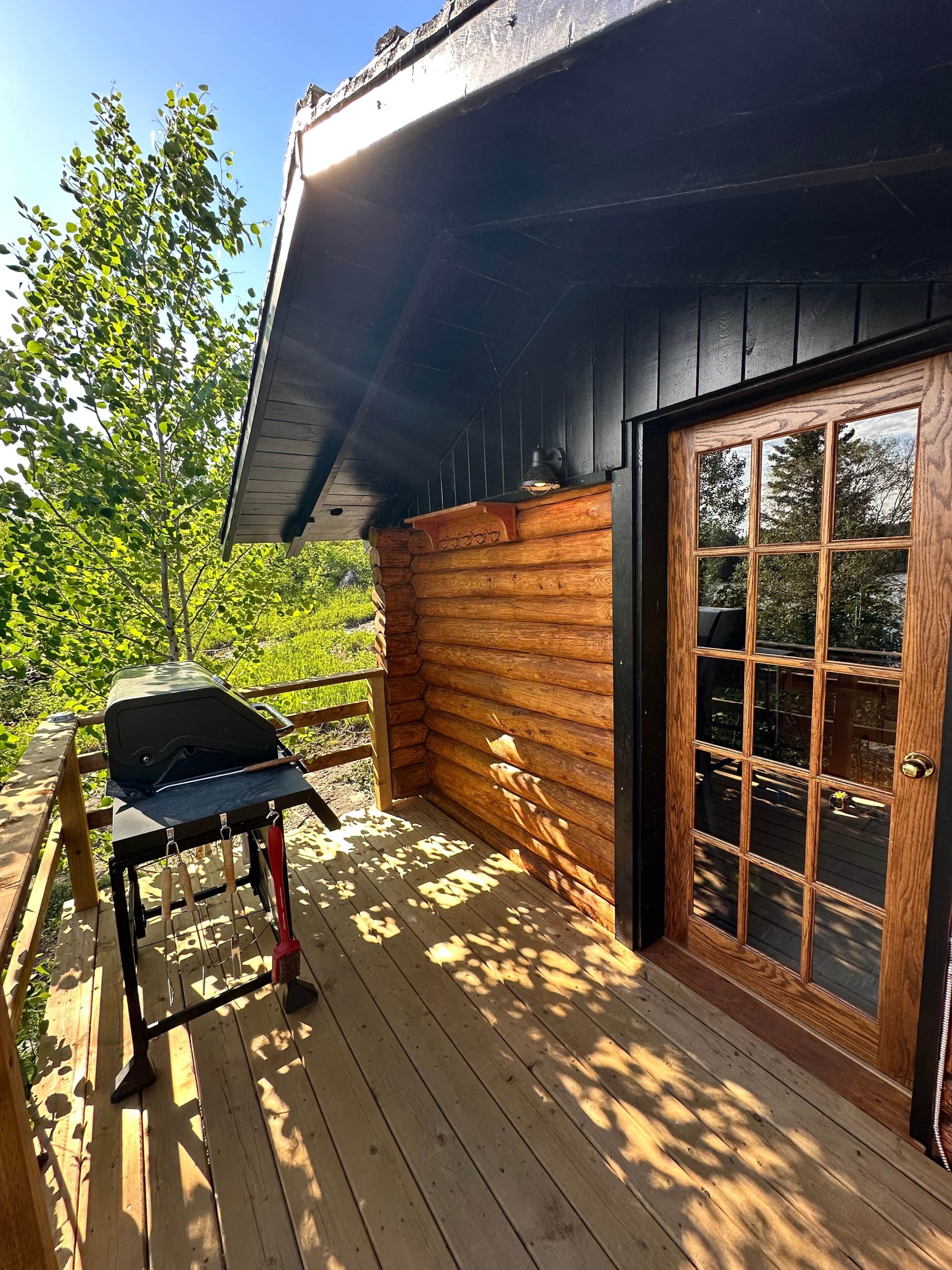 Une terrasse en bois avec un barbecue, une porte à panneaux de verre et une vue sur la verdure.