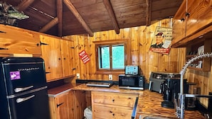 Eine Holzhüttenküche mit Kühlschrank, Mikrowelle, Toaster, Spüle und einem Fenster mit Blick auf Grün.