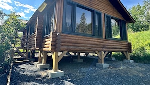 Eine Blockhütte mit großen Fenstern, einer Holzterrasse und einem Kiesgrundstück.