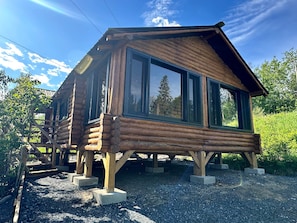 Una cabaña de troncos con ventanas amplias, una terraza de madera y suelo de grava.