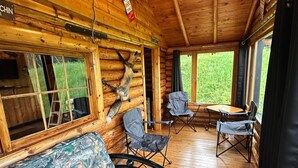 Ein Holzfußboden, eine Couch mit Tarnmusterstoff und ein Fenster mit Blick auf Grünpflanzen.