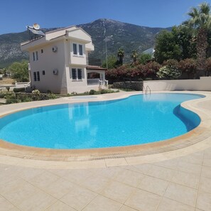 A swimming pool with a curved edge, a white building with a balcony, and a mountainous backdrop. - Beautiful 2-bedroom apartment with AC in charming Fethiye (Fethiye)