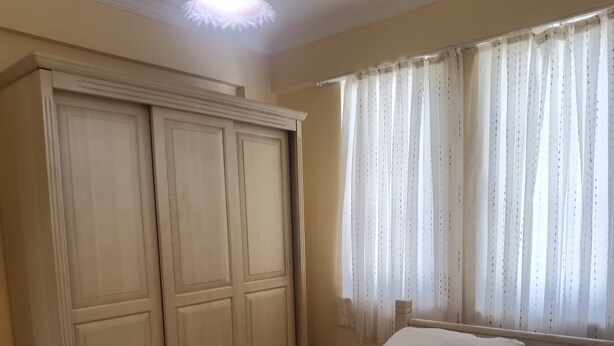 Quarto com um guarda-roupa grande, cama com roupa de cama branca e janela com cortinas leves.