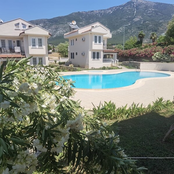A two-story building with a swimming pool, surrounded by greenery and mountains.