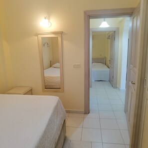 Une chambre à coucher comprenant un lit, une table de chevet, un miroir et une porte donnant sur une autre pièce.