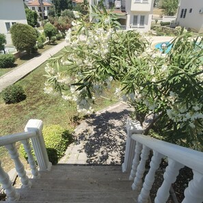 A staircase leading to a balcony with white railings, surrounded by greenery and a pool.