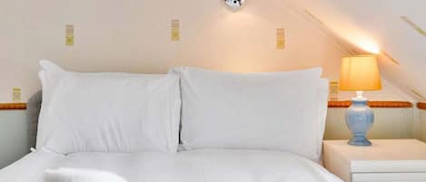 A bedroom with a bed, pillows, a nightstand, a lamp, and a wall-mounted light fixture.