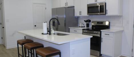 A modern kitchen with white cabinetry, stainless steel appliances, and a central island with bar stools.