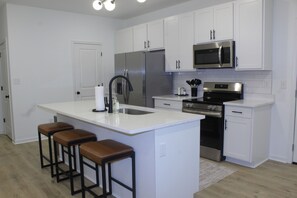 A modern kitchen with white cabinetry, stainless steel appliances, and a central island with bar stools. - Luxury 2BR Near Medical District - Gated Parking & Sleeps 6 (Memphis)