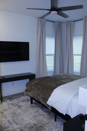 Ein Schlafzimmer mit einem Bett, einem Schreibtisch, einem an der Wand montierten Fernseher und einem Deckenventilator.