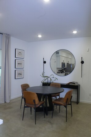 A modern dining area with a round table, four chairs, a potted plant, and a large mirror on the wall. - Luxury 2BR Near Medical District - Gated Parking & Sleeps 6 (Memphis)