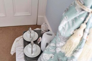 A small table with a tray containing a teapot, cups, and a sugar bowl, a jar, and a white appliance, possibly a coffee maker, on a patterned fabric backdrop. - GuestReady - Bright Studio in Leith, Edinburgh (Edinburgh)