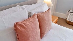 Un letto con cuscini bianchi e rosa, una testiera grigia e un comodino con una lampada.