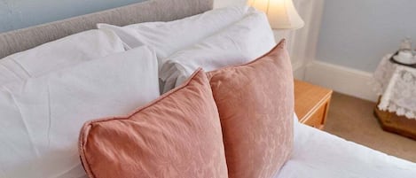 A bed with white and pink pillows, a grey headboard, and a bedside table with a lamp.