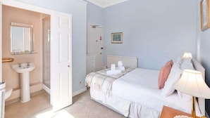 Una camera da letto con un letto, un comodino, una lampada e un bagno con lavandino e specchio.