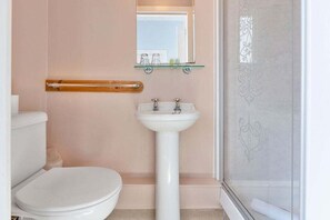 A bathroom with a toilet, a pedestal sink, a glass shelf above the sink, and a shower area. - GuestReady - Bright Studio in Leith, Edinburgh (Edinburgh)