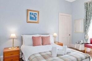 A bedroom with a bed, two bedside tables, a nightstand, a framed picture, a door, and a window with curtains. - GuestReady - Bright Studio in Leith, Edinburgh (Edinburgh)