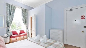 Camera d'albergo con un letto, una cassettiera, una sedia rossa, una finestra con tende e una porta con cartello ‘divieto di fumo’.
