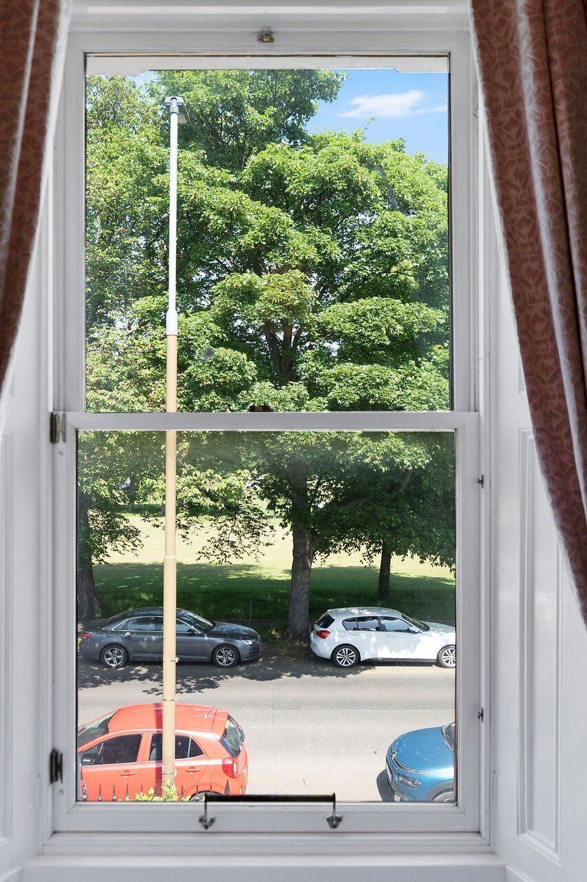 A window with a view of a parking lot and trees.