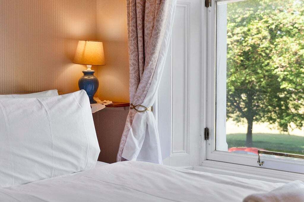 Una habitación de hotel con una cama, una lámpara, una ventana con vistas a árboles y una cortina.