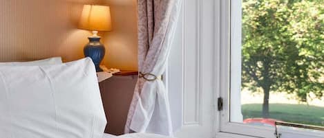 Una habitación de hotel con una cama, una lámpara, una ventana con vistas a árboles y una cortina.