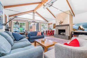 A spacious living room with a high ceiling, a fireplace, and a view of the outside. - Beach House w/ AC, Steps to Sand, 38th St Park, and the Boardwalk (Newport Beach)