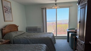 Hotelkamer met twee bedden, een dressoir, een plafondventilator en een balkon met uitzicht.