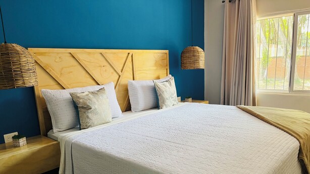 Una cama con cabecera de madera, ropa de cama blanca y dos mesitas de noche con lámparas.