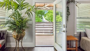 Habitació amb una planta en test, un ventilador de sostre, una porta corredissa de vidre que dona a una terrassa i una taula de fusta petita.
