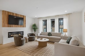 Ein modernes Wohnzimmer mit Flachbildfernseher, Kamin, Sofa, Sesseln und Couchtisch.