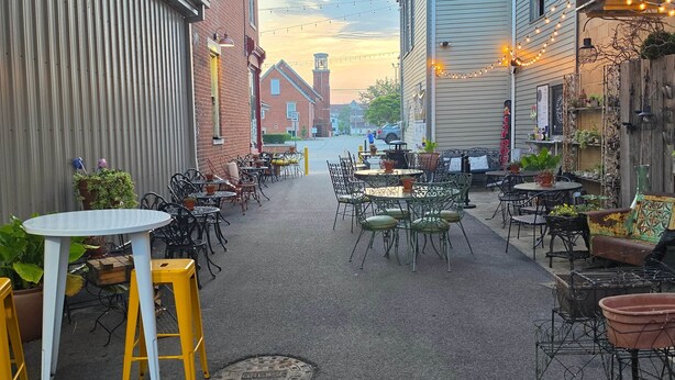 Un espace extérieur aménagé avec des tables et des chaises, entouré de bâtiments et offrant une vue sur la rue.