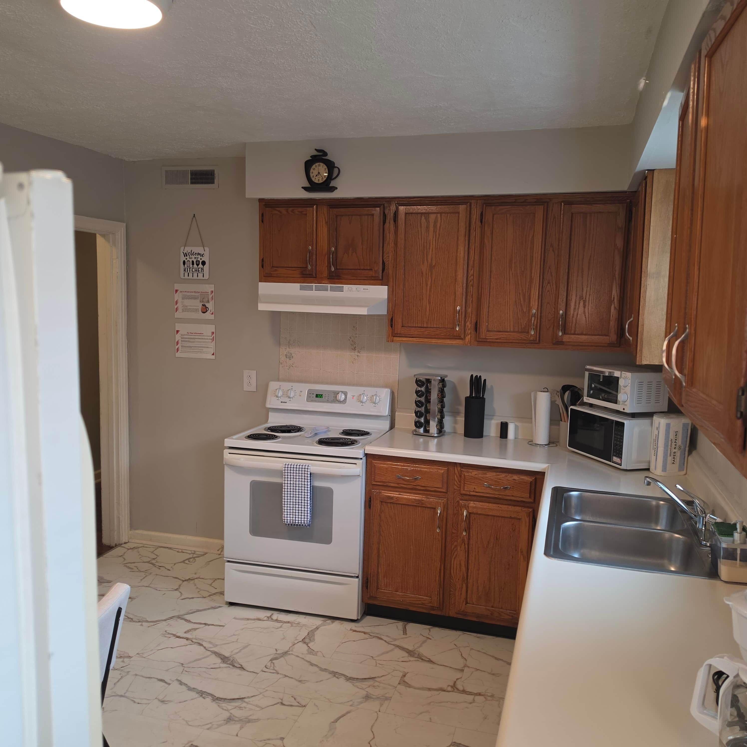 A kitchen with wooden cabinets, a white stove, a microwave, and a sink.