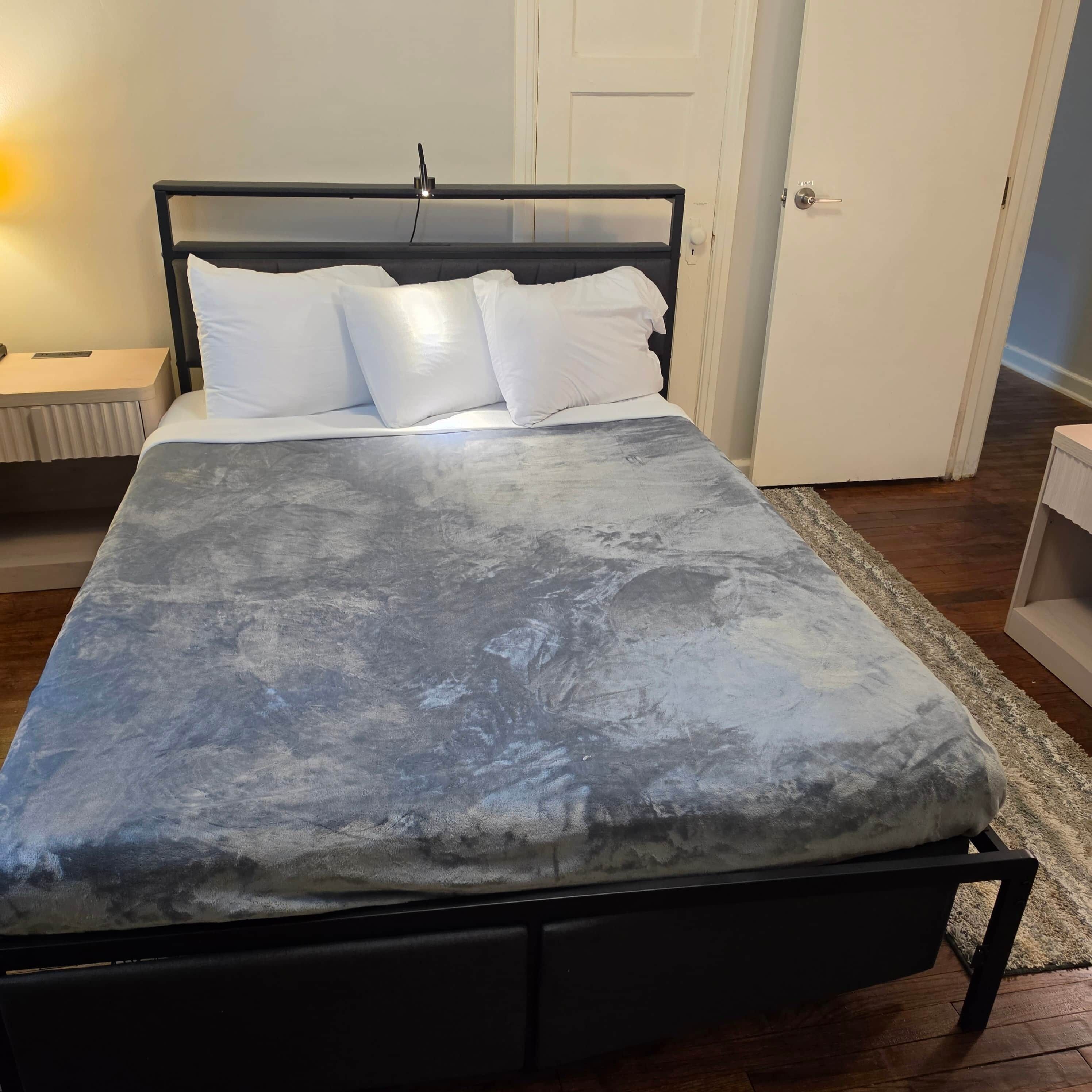 Ein Bett mit grauer, strukturierter Bettdecke, weißen Kissen und einem schwarzen Metallgestell.