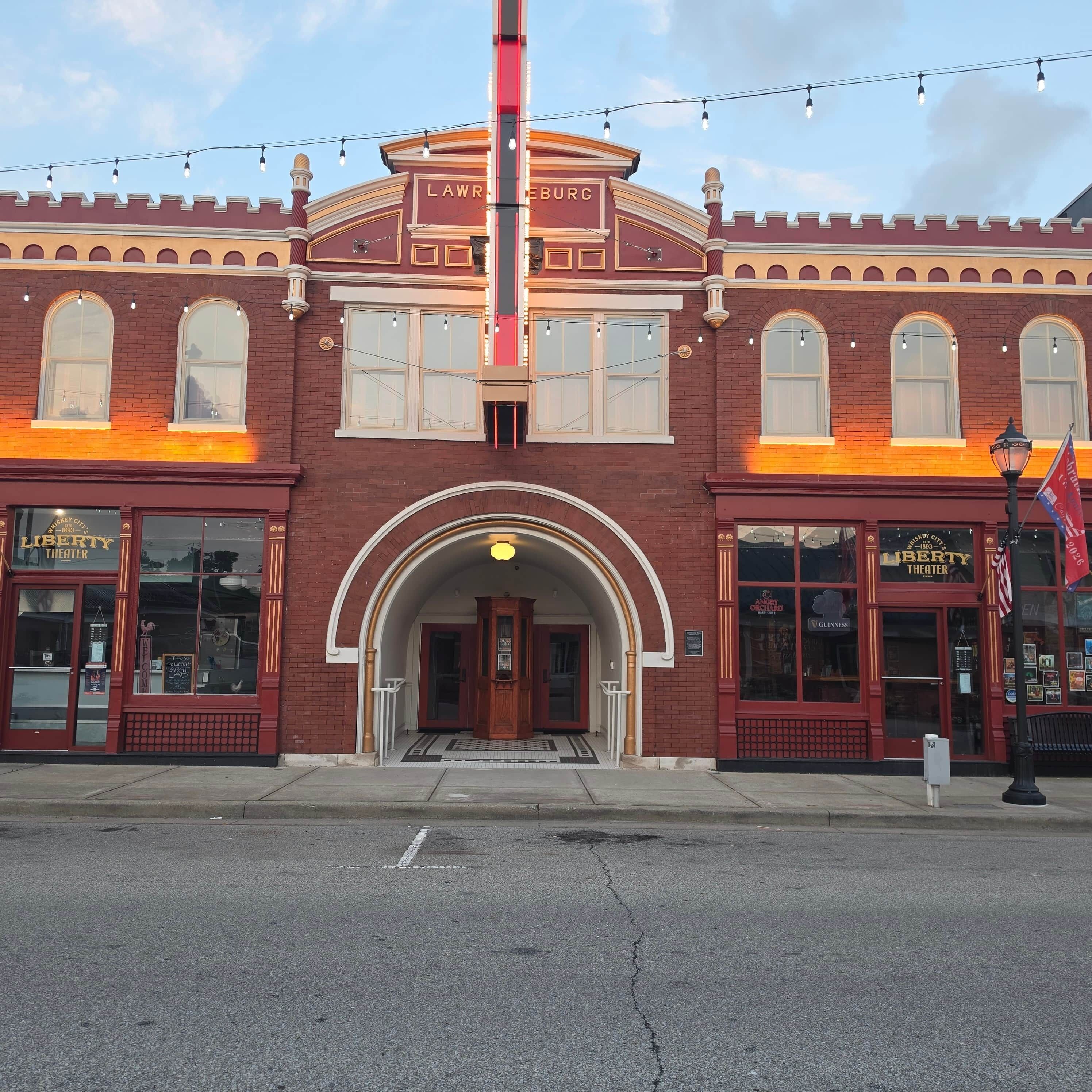 Un théâtre historique à la façade rouge, doté d’une entrée en arc de cercle et d’une enseigne lumineuse.