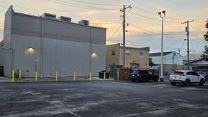 Un parking avec un grand bâtiment industriel, quelques voitures et des poteaux électriques.