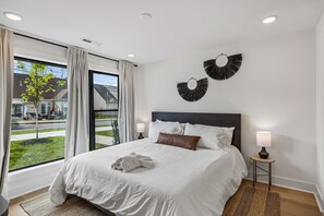 Ein modernes Hotelzimmer mit einem großen Bett, Blick auf die Straße und zwei Wanddekorationen.