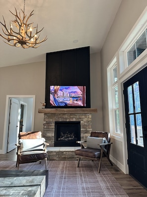 A living room with a fireplace, a television mounted above it, and a large window.