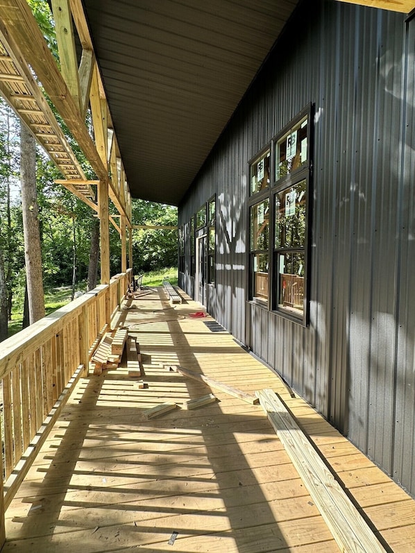A covered wooden deck with a bench, large windows, and a view of the surrounding forest.