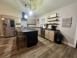 A modern kitchen with a central island, stainless steel appliances, and wooden flooring.