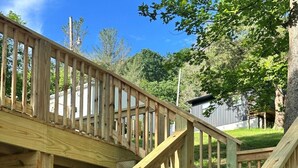 A wooden outdoor staircase with a railing, surrounded by greenery and trees. - Brand new creekside home with hot tub, private dock and boat ramp! (Gallipolis)