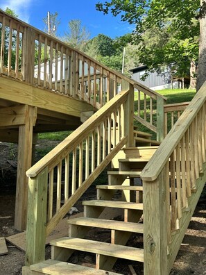 A wooden outdoor staircase with a railing, surrounded by greenery and trees.